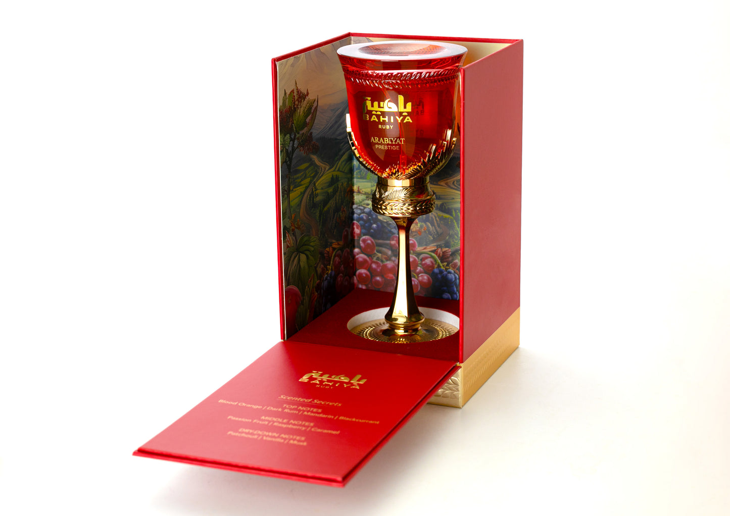 A luxurious red and gold goblet filled with red liquid sits in an ornate box with fruit illustrations, evoking the fruity scent of ARABIYAT PRESTIGE - BAHIYA RUBY 3.4FL.OZ EDP SPRAY FOR WOMEN AND MEN, its open lid displaying elegant gold text.