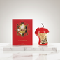 Red apple-shaped container with gold accents next to a red box featuring an illustration of Adam and Eve, labeled 'Forbidden'.
